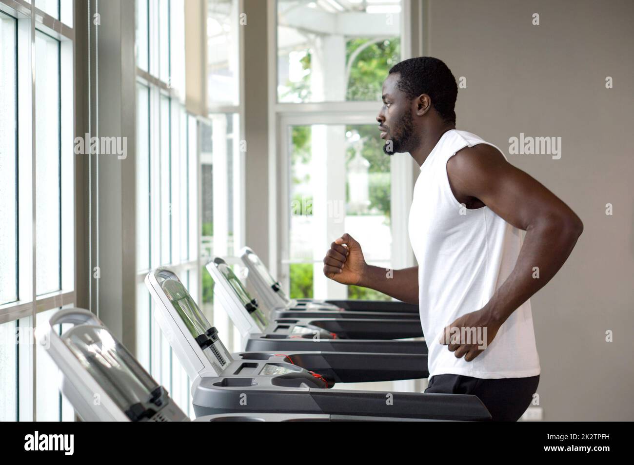 Young short curly black hair man with moustache and beard running on a treadmill in the gym, looking out of the window. Stock Photo