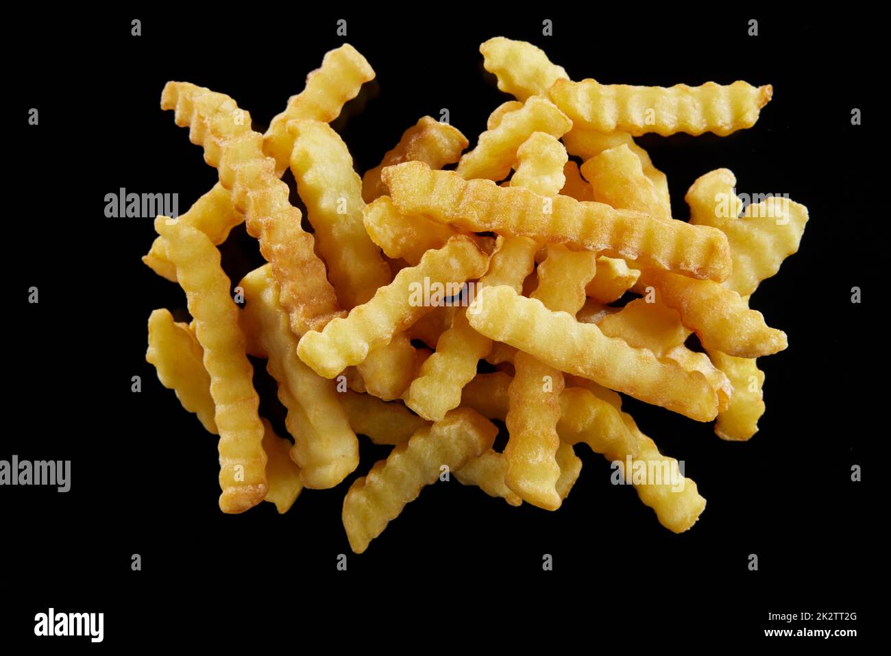 Pile of tasty crinkle cut fried potatoes on black surface Stock Photo