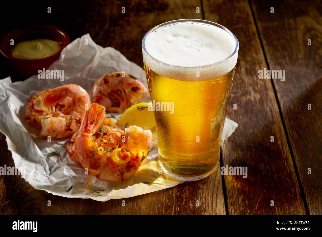 Cold pint of lager in a glass with grilled herbal prawns Stock Photo