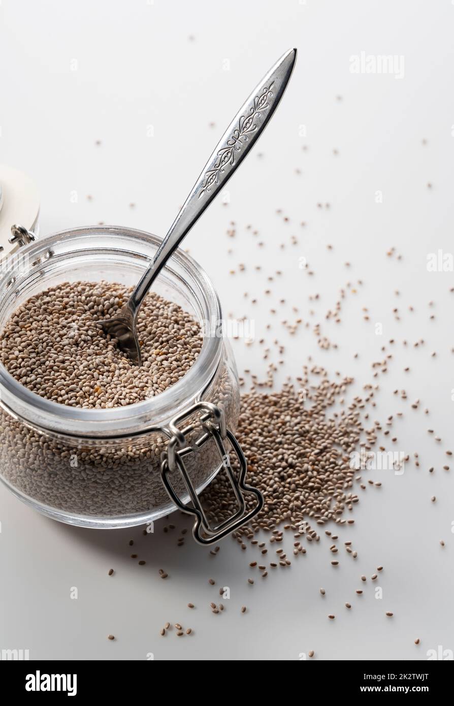 Glass container with spoon and white chia seeds placed on white ...