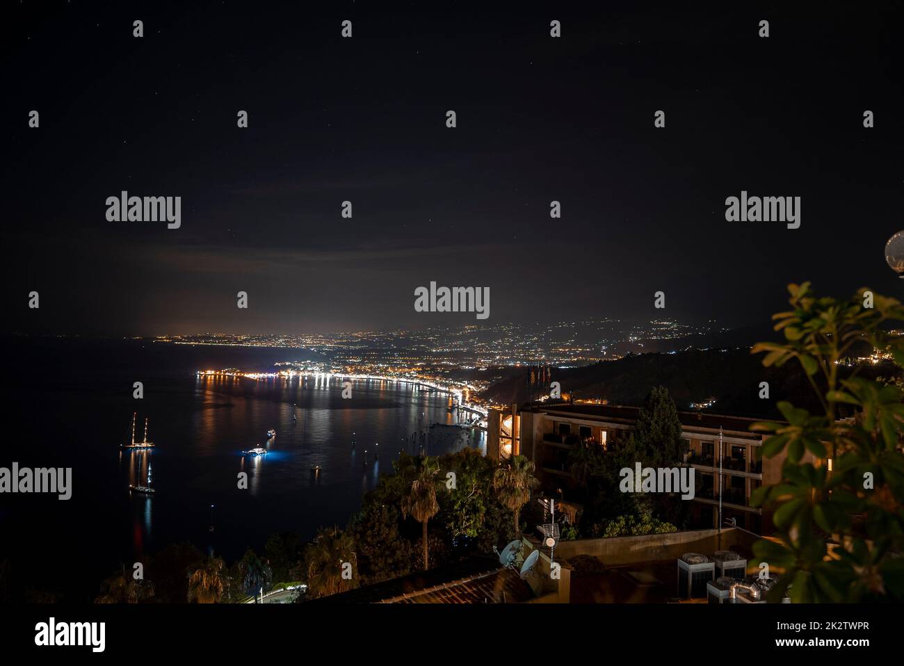 Idyllic view of Hotel Elios and Mount Etna at illuminated coast by sea in night Stock Photo