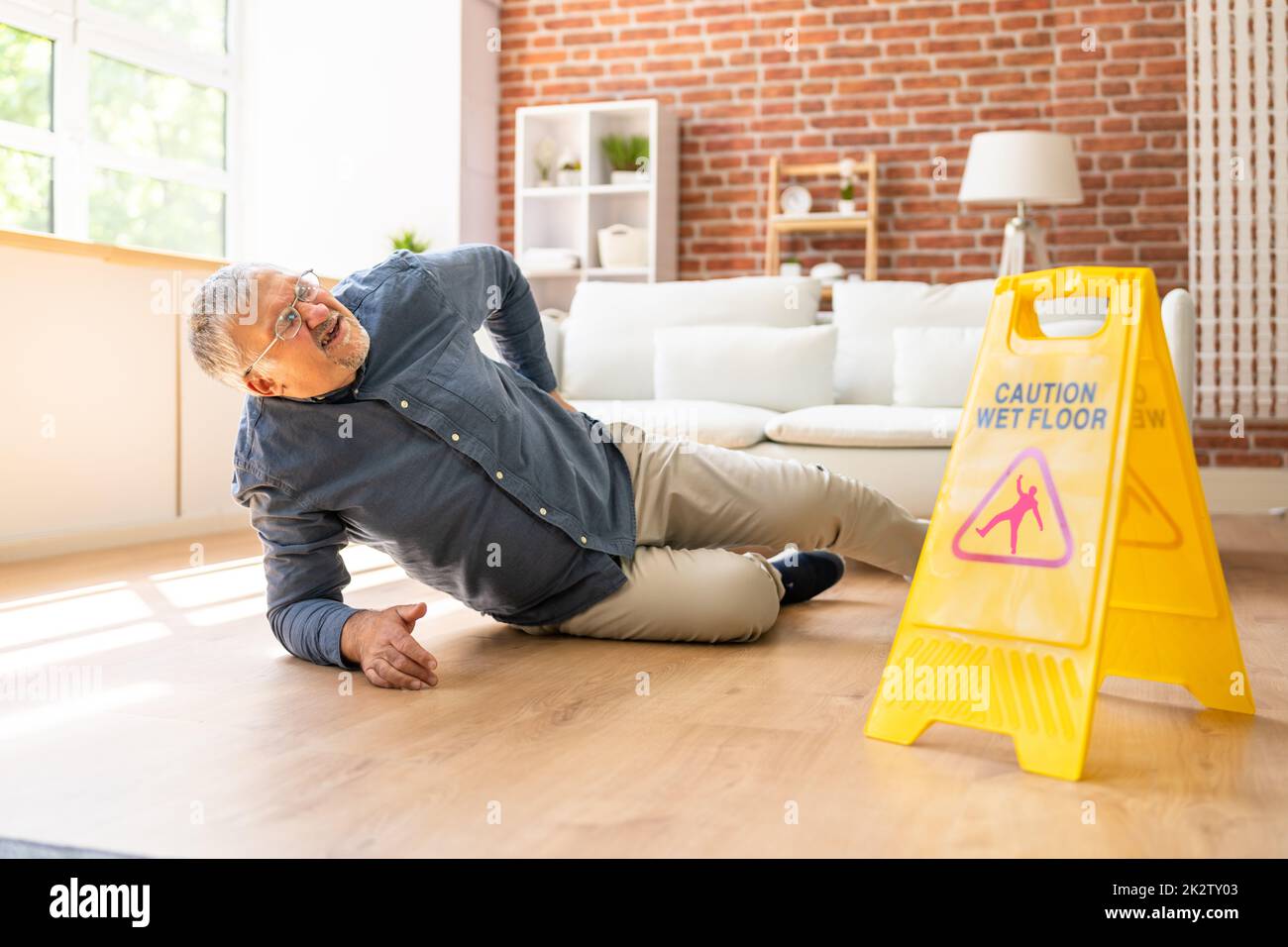 Man Falling On Wet Floor In Front Of Caution Sign Stock Photo