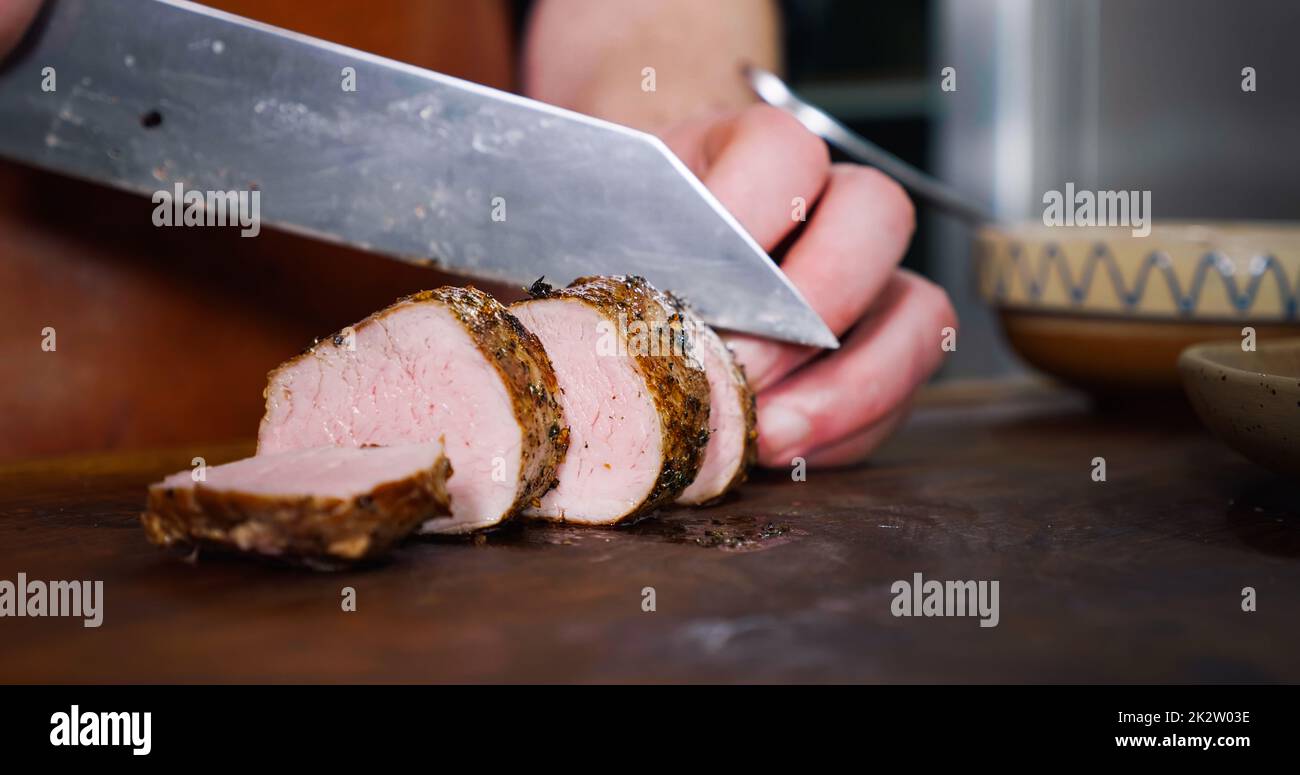 Chef Cuts Juicy Pork Steak on Rustic Cutting Board on Wooden Background. Stock Photo