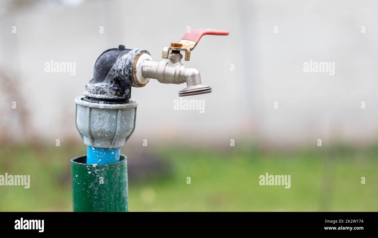 Water faucet on the background of nature. Opening or closing a faucet to save water indicates a water shortage problem. Rustic fountain with daylight. Selective focus with blurred background. Stock Photo