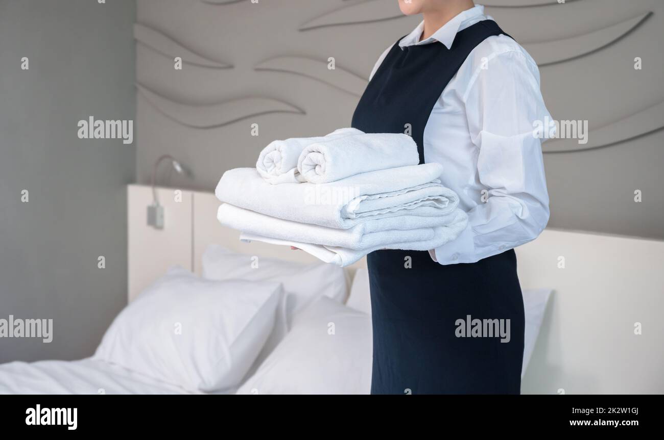 Room service maid holding clean folded white towels in hotel guest room