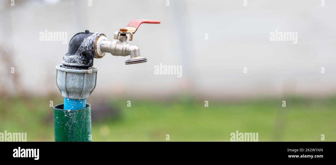 Water faucet on the background of nature. Opening or closing a faucet to save water indicates a water shortage problem. Selective focus with blurred background. Banner with copy space. Stock Photo