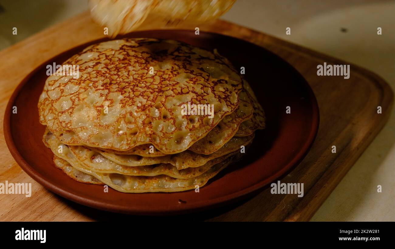 A stack of hot pancakes. Man put pancake on top. Pancakes with holes. Pancake week. Ukrainian, Russian tradition. Stock Photo