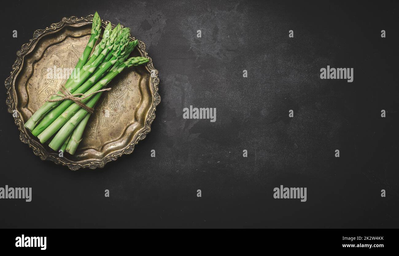 Fresh green asparagus sprouts on a round copper plate, black background. View from above Stock Photo