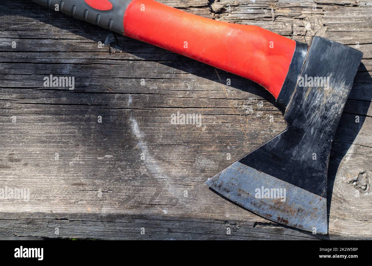 A sharp ax with an ergonomic rubberized handle on a wooden background. The ax is intended for rough, rough processing of wood. Has a forged heat treated carbon steel wedge. Stock Photo