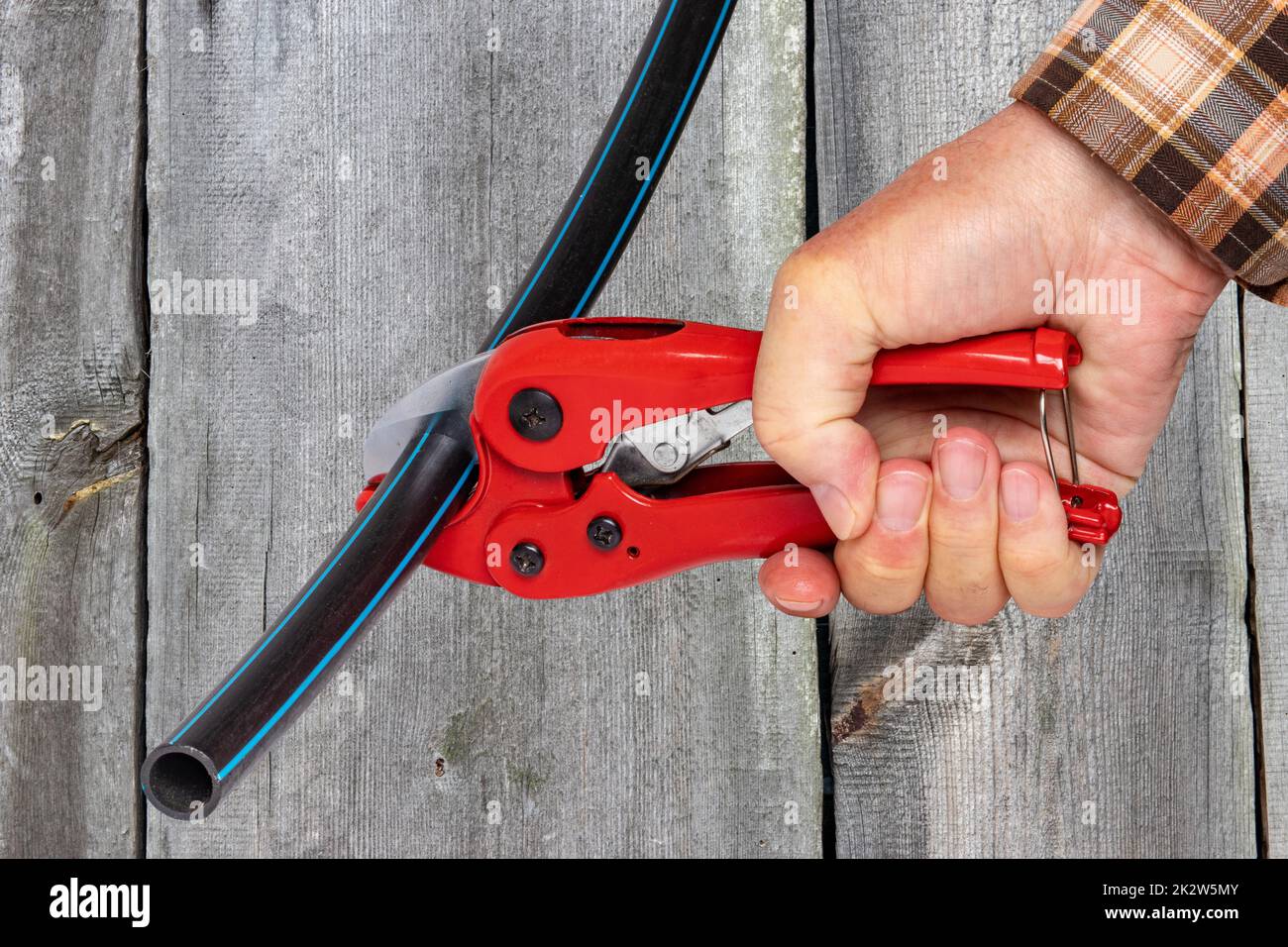Craftsman tools. A man accurately cuts a piece of PE pressure pipe or water pipe with a red pvc