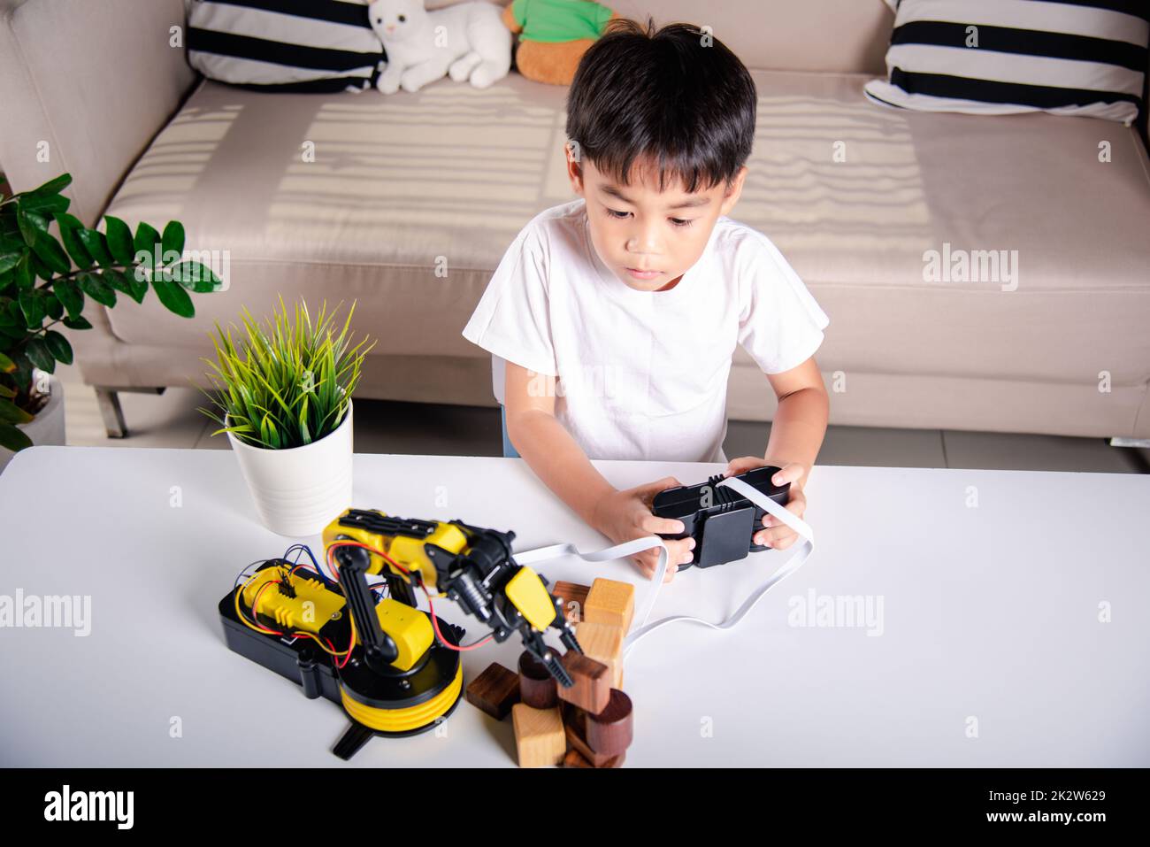 Happy Asian little kid boy using remote control playing robotic machine arm for pick up wood block Stock Photo