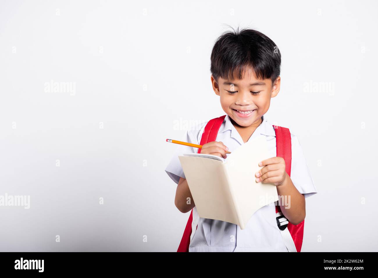 Asian toddler smiling happy wear student thai uniform red pants holding pencil for writers notebook Stock Photo