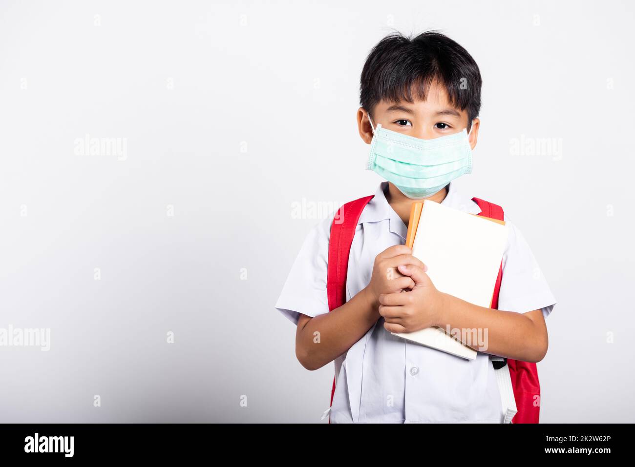 Asian student kid boy wearing student thai uniform and medical protect face mask and hugging note Stock Photo