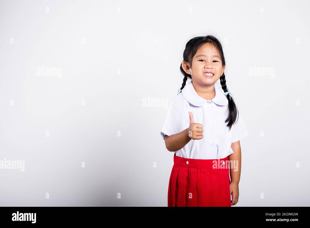 Asian adorable toddler smiling happy wear student thai uniform red skirt show thumb up finger Stock Photo