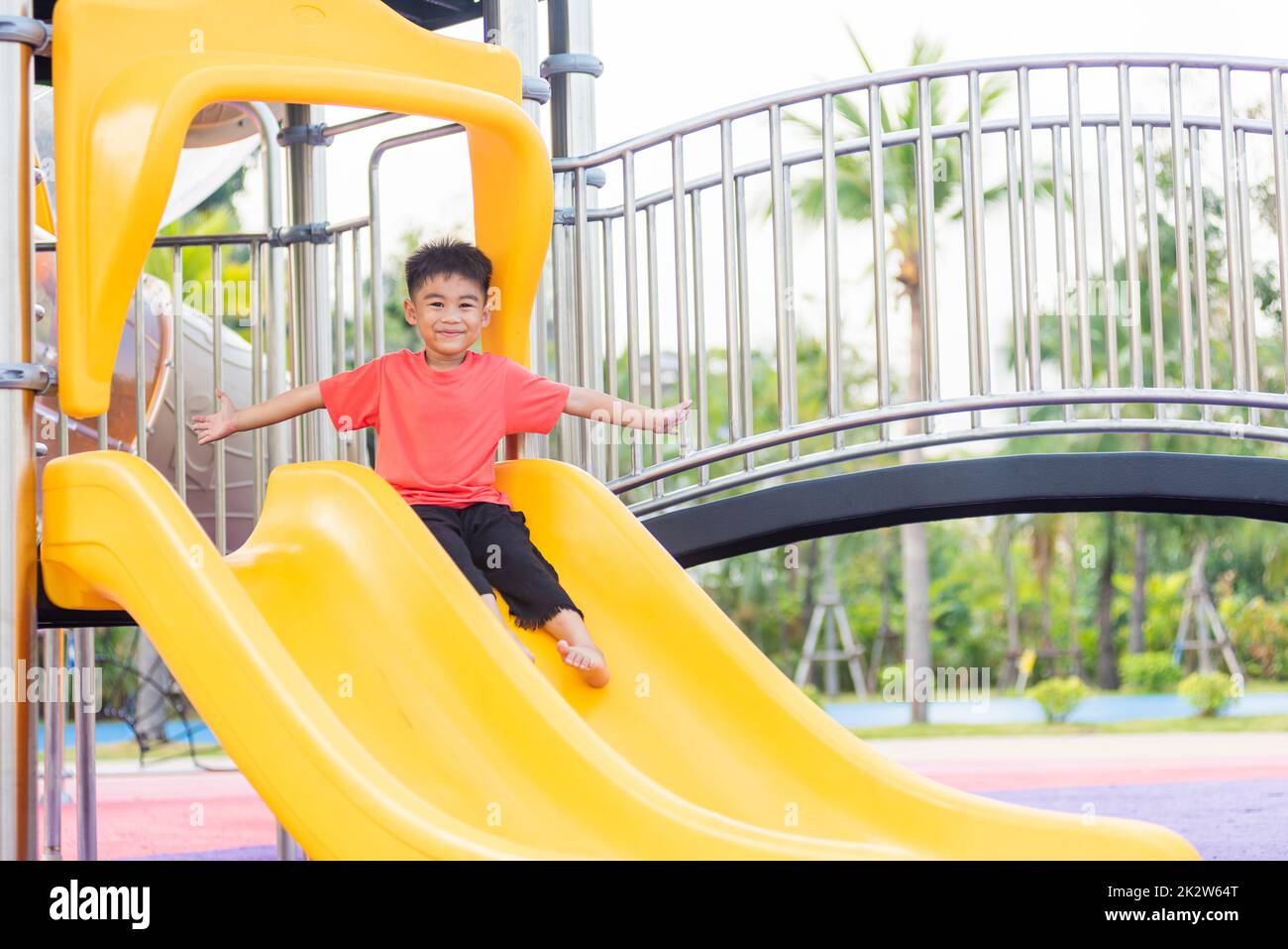 Asian child smiling playing on slider bar toy outdoor playground, happy preschool little kid having funny while playing on the playground equipment in the daytime in summer, Little boy climbing Stock Photo