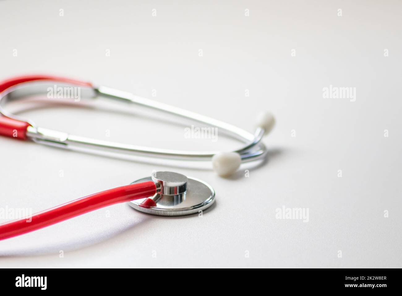 Red stethoscope in doctors office for professional cardio checkup and healthy heartbeat pulse check by cardiologist in clinical treatment room on white desk as medical equipment to measure body params Stock Photo