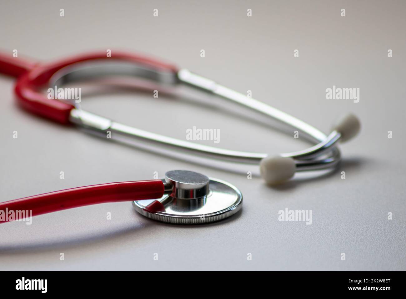 Red stethoscope in doctors office for professional cardio checkup and healthy heartbeat pulse check by cardiologist in clinical treatment room on white desk as medical equipment to measure body params Stock Photo