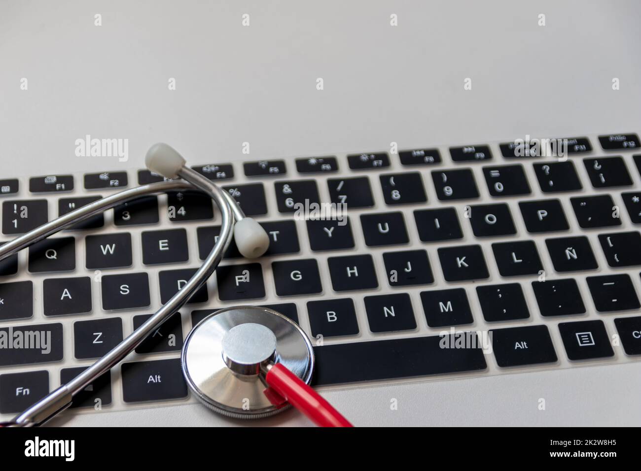 Red stethoscope on black computer keyboard on white desk shows digital doctors office with digital patient records for medical diagnosis and cardiology measurement with antivirus checkup hacker attack Stock Photo