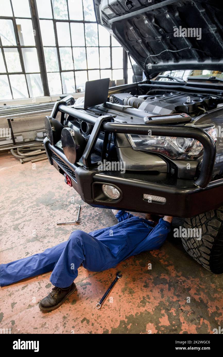 Male auto mechanic in coveralls working under modified SUV in garage