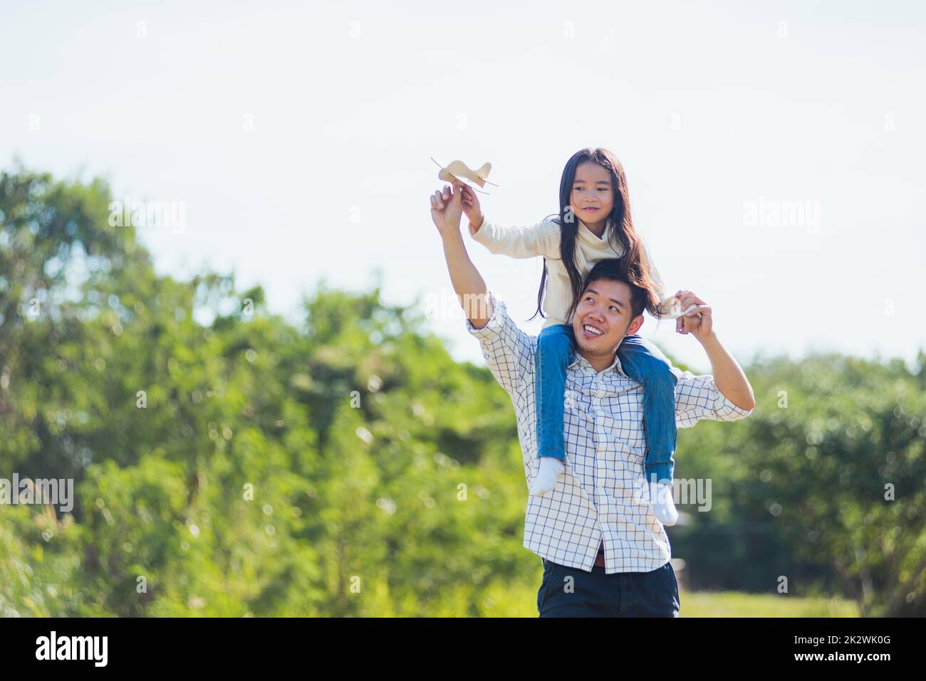 father and carrying an excited girl on shoulders having fun and enjoying outdoor lifestyle together playing aircraft toy Stock Photo