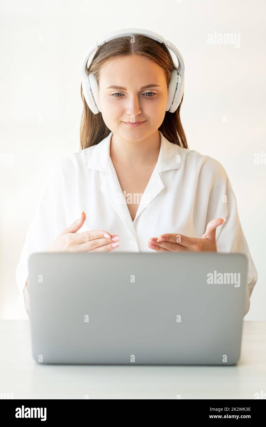 Remote education. Zoom videochat. Virtual meeting. Freelance job. Confident female teacher in white wireless headphones giving online lesson working f Stock Photo