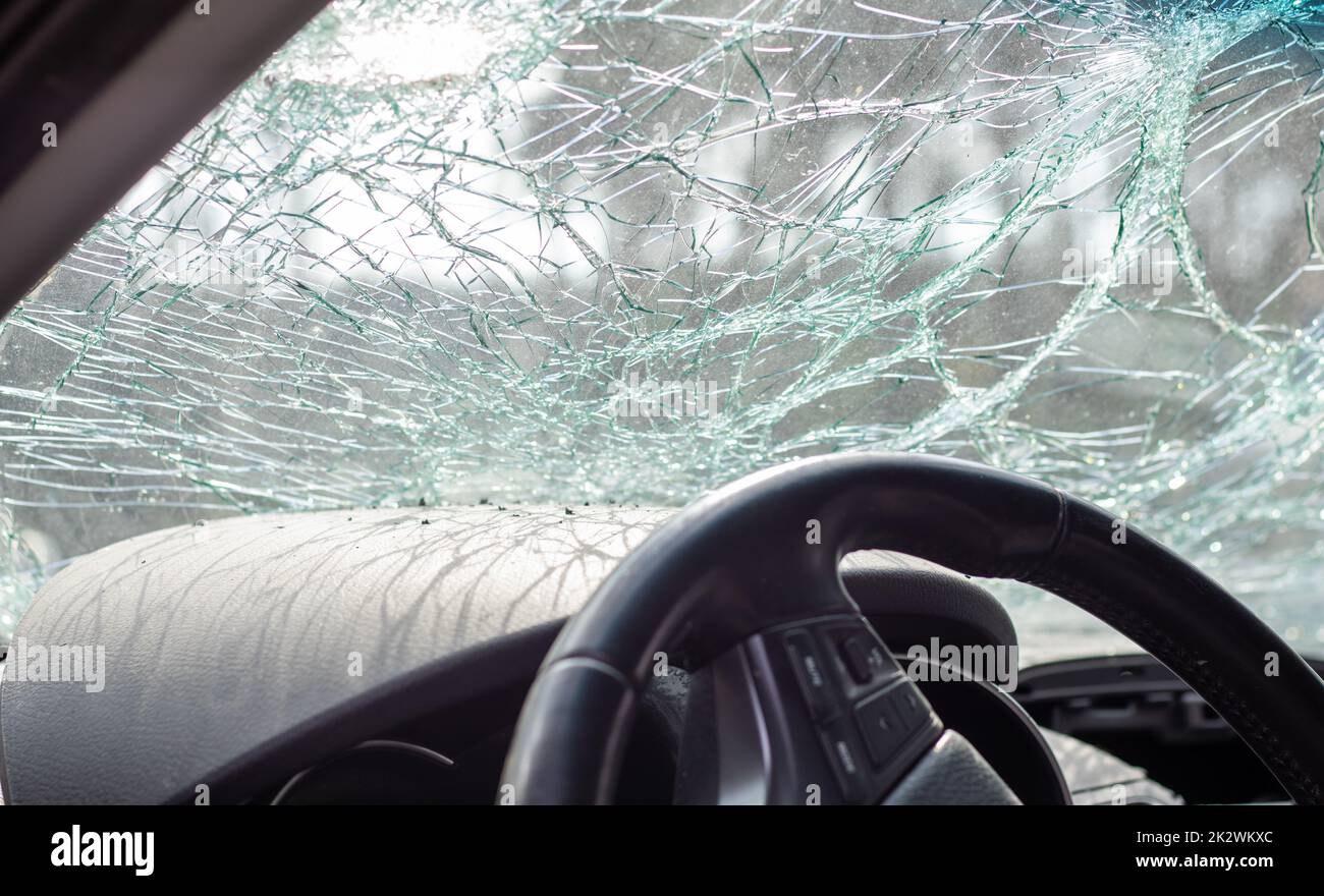 Damaged car window after an accident. Broken windshield as a result of an accident, inside view. Cabin interior details, view from the cab. Safe movement. Broken windshield. Glass crack and damage. Stock Photo