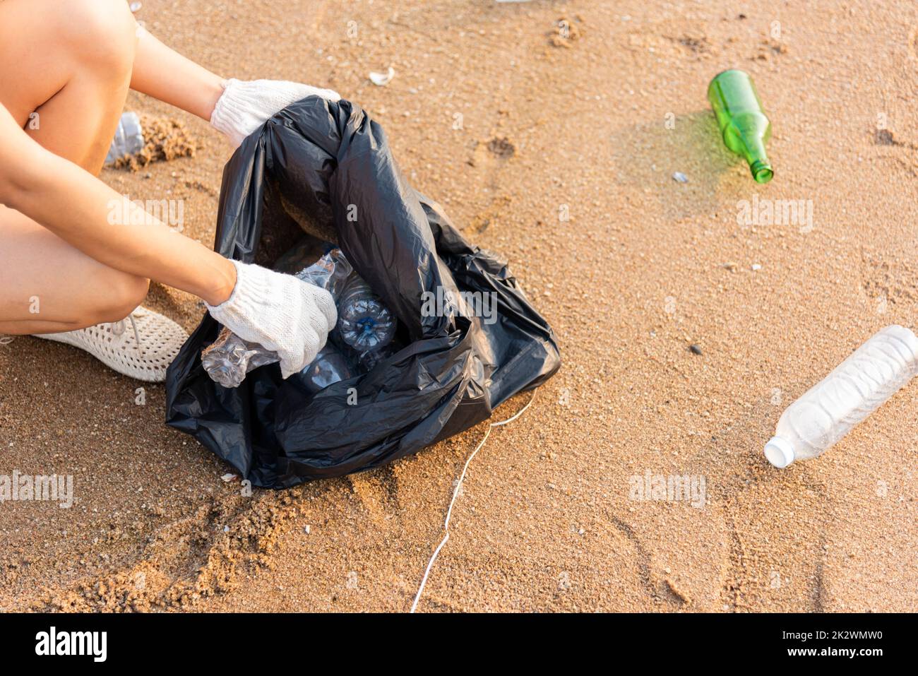 Volunteer woman picking plastic bottle into trash plastic bag black for