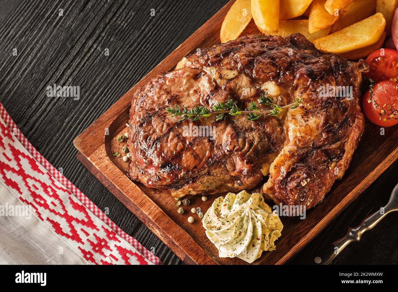 Ribeye steak with potatoes, onions and baked cherry tomatoes. Juicy steak with flavored butter