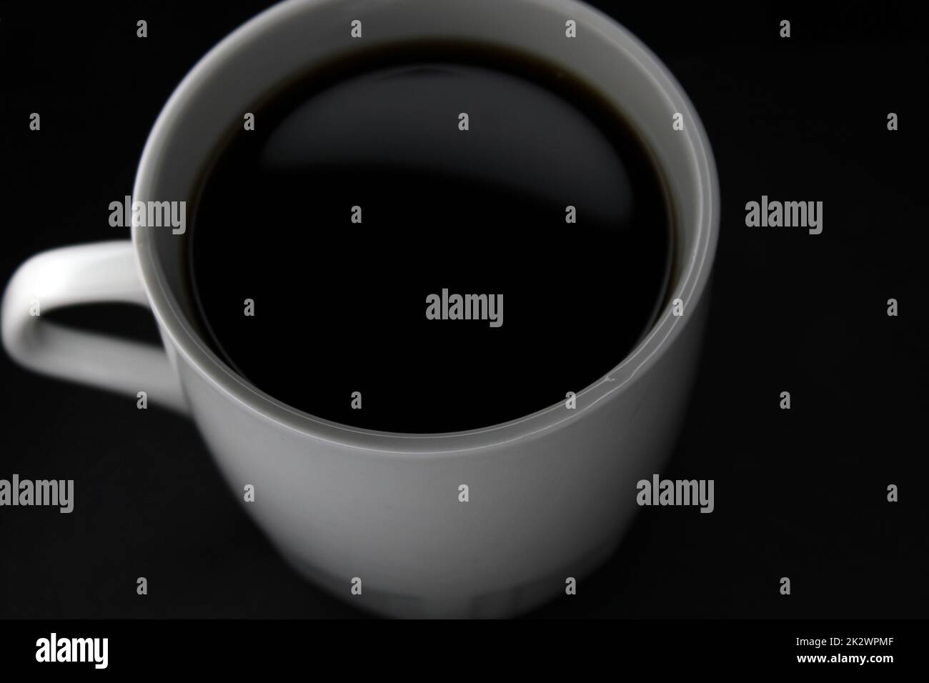 White mug with black coffee on a black background. View from above. Close-up. Stock Photo
