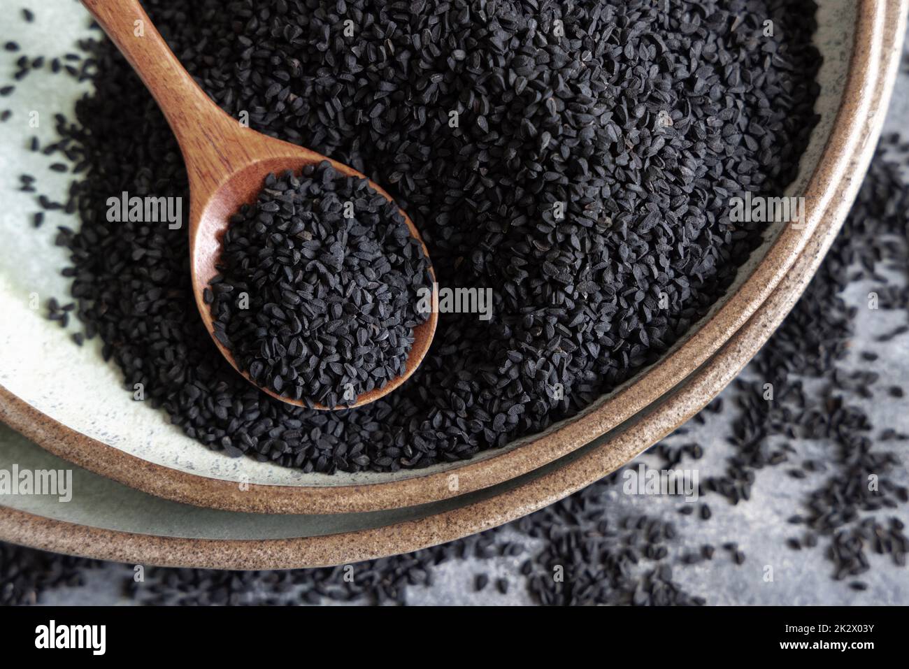 Plate of Indian spice Black cumin (nigella sativa or kalonji) seeds close up with a wooden spoon Stock Photo