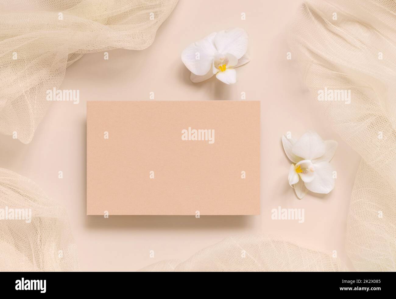 Blank card near white orchid flowers and tulle on light yellow top view