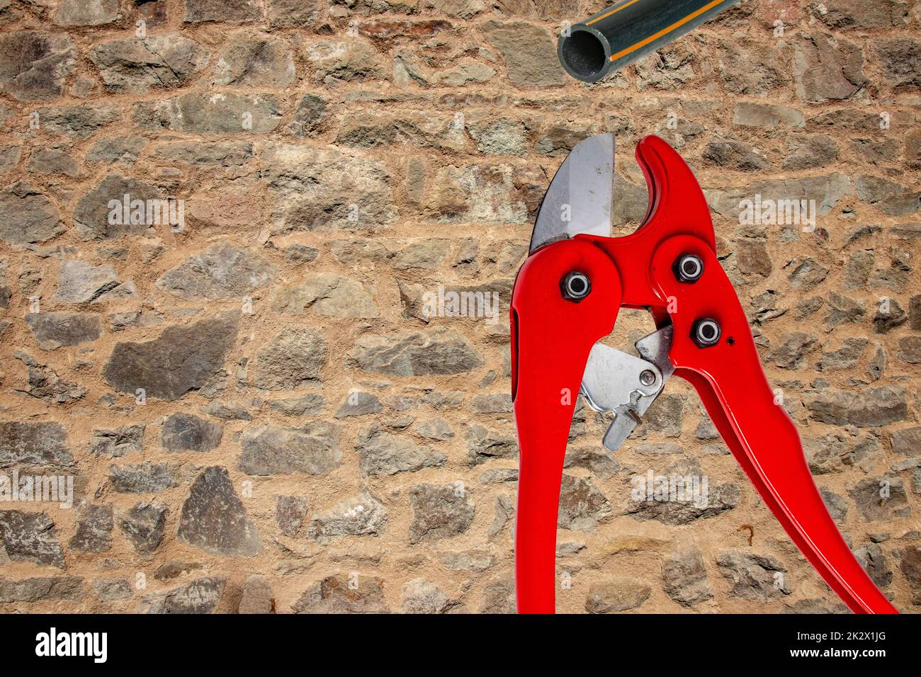 Plumber tools isolated. A red PVC pipe cutter for cutting plastic pipes and a piece of PE pressure pipe or water pipe over stone wall. Space. Craftsman tools. Stock Photo