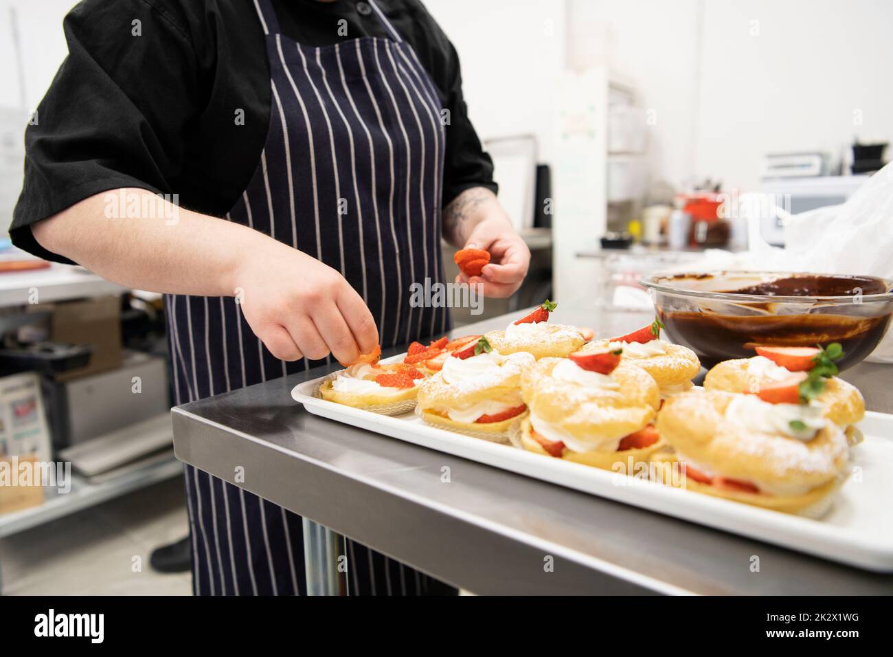 Female baker topping French pastries with strawberries in bakery Stock