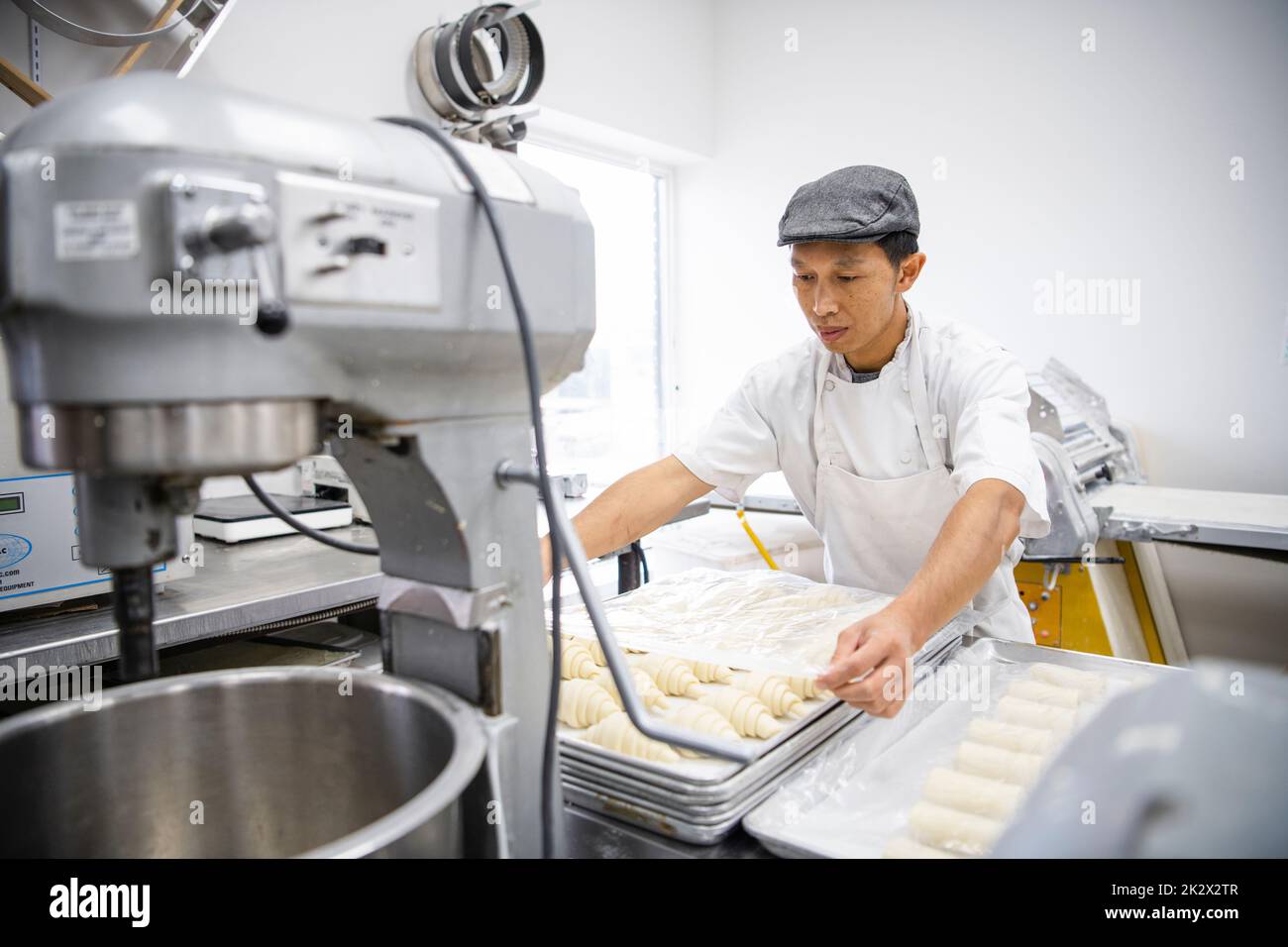 Male baker covering croissant dough with plastic wrap in bakery Stock