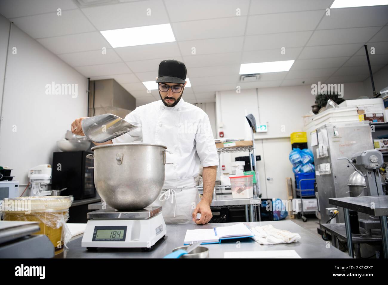 Male baker measuring ingredients at scale in commercial bakery kitchen Stock Photo Alamy