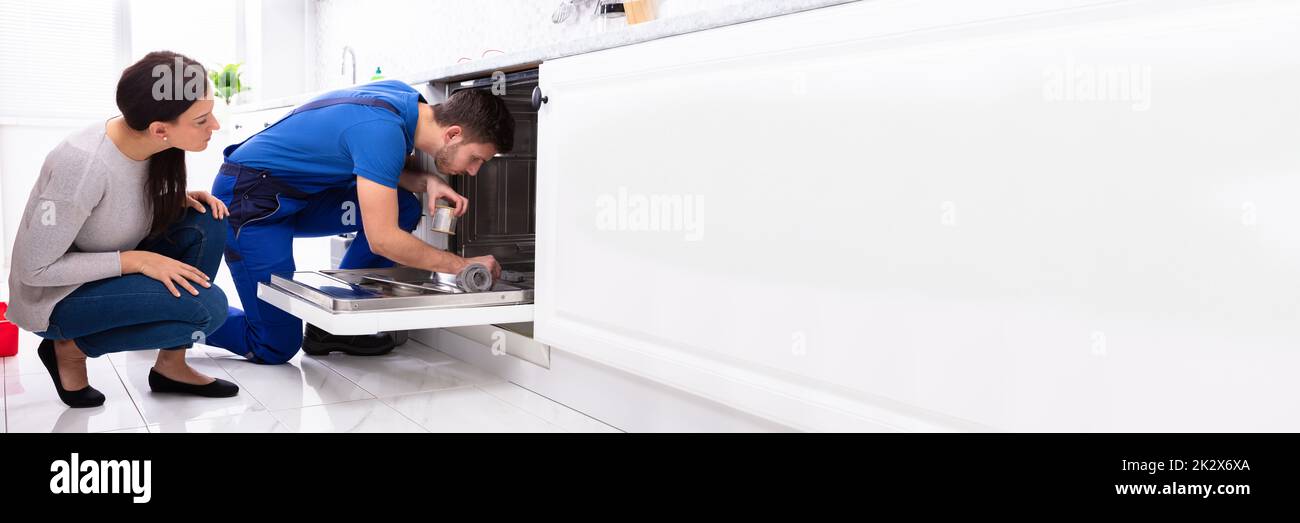 Woman Looking At Repairman Repairing Dishwasher In Kitchen Stock Photo