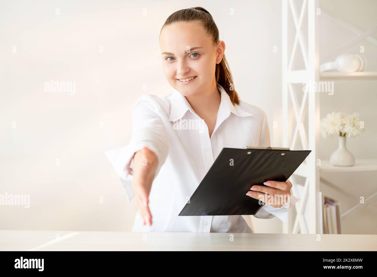 Business contract. Partnership agreement. Professional cooperation. Confident cheerful woman with clipboard greeting client with handshake at light mo Stock Photo