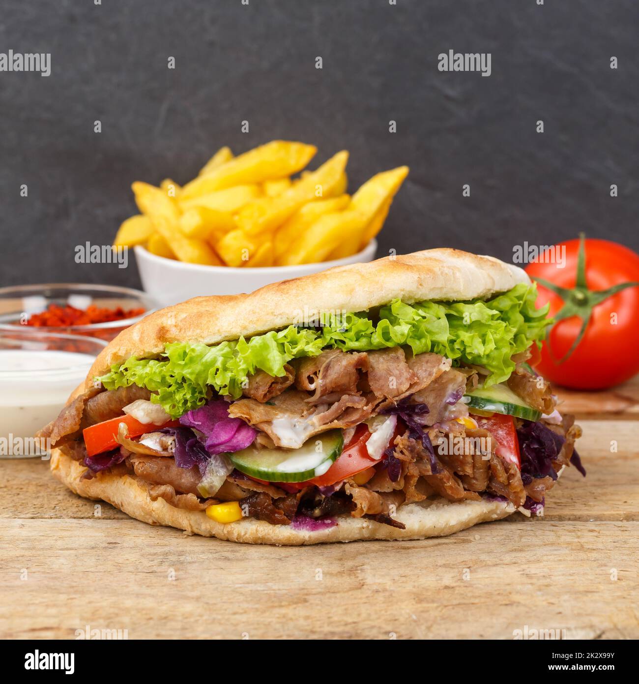 Döner Kebab Doner Kebap fast food in flatbread with fries on a wooden board square snack Stock Photo