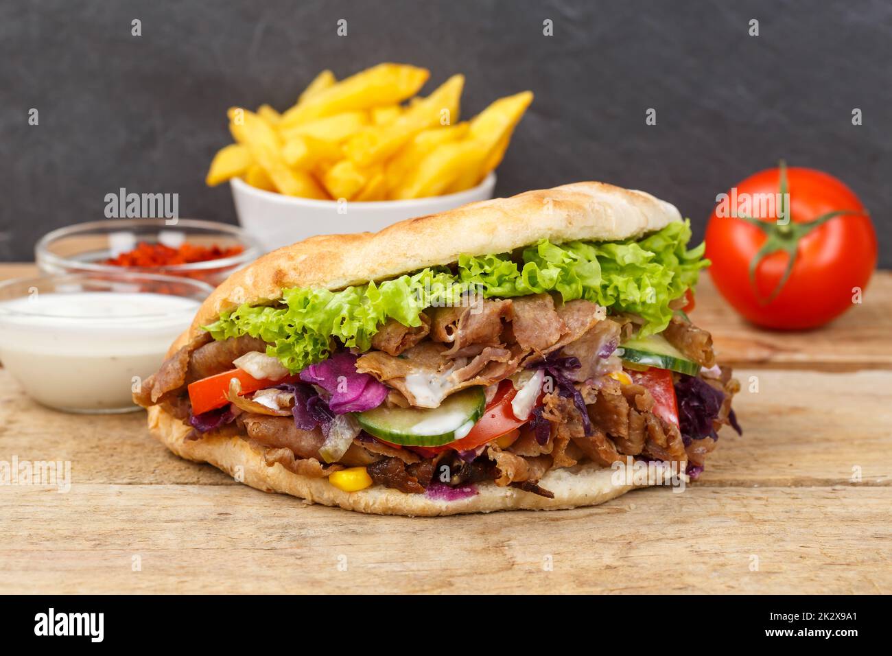 DÃ¶ner Kebab Doner Kebap fast food in flatbread with fries on a wooden board Stock Photo