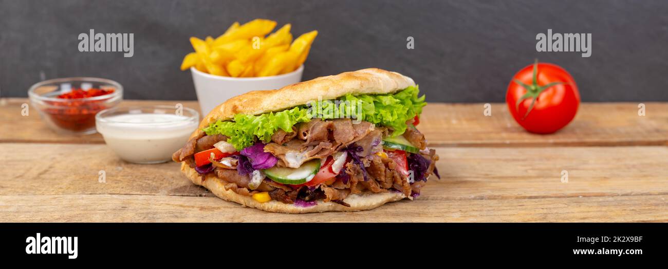 Döner Kebab Doner Kebap fast food in flatbread with fries on a wooden board panorama snack Stock Photo