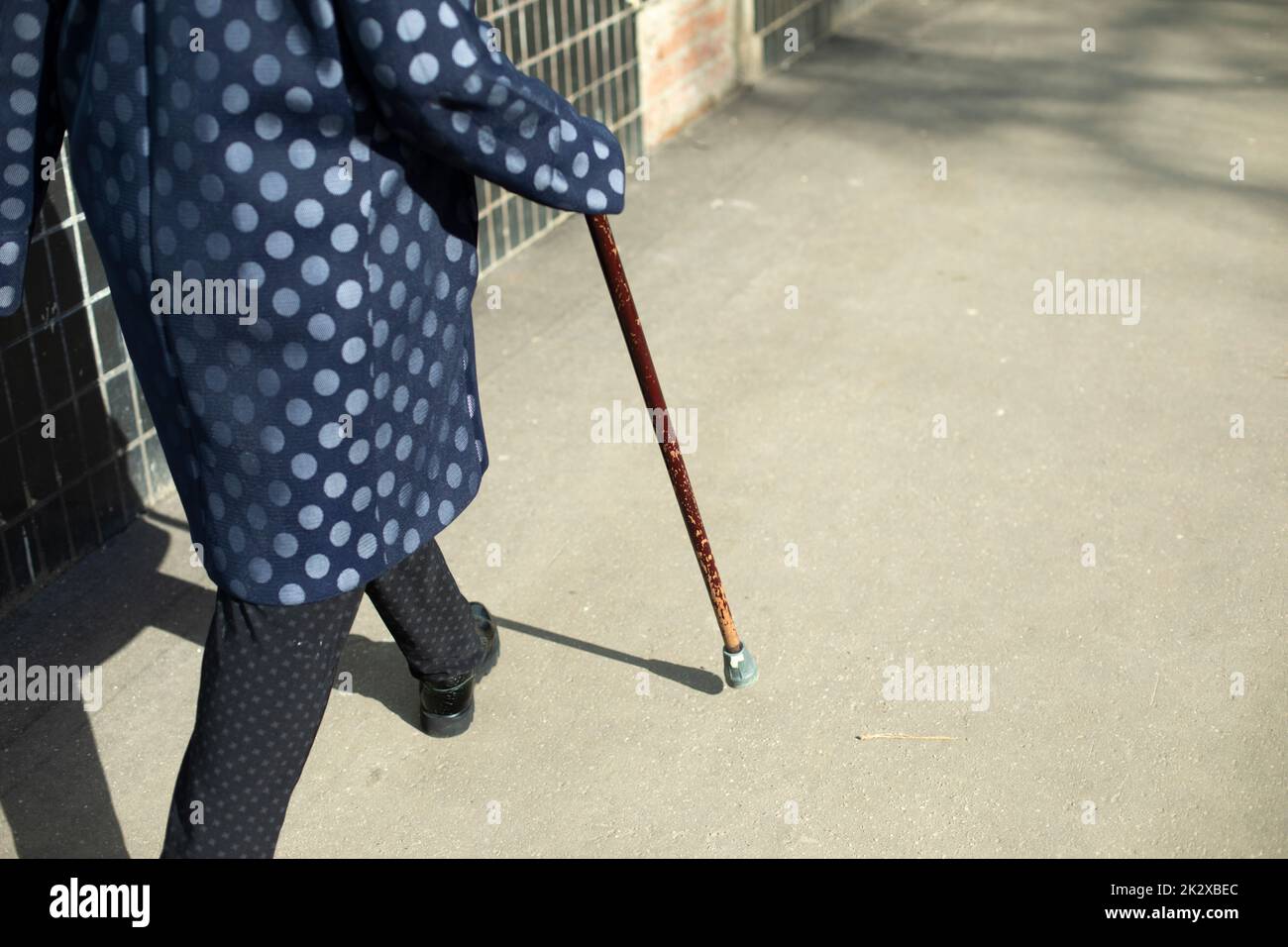 Grandma with walking stick. Woman walks on asphalt. Stock Photo