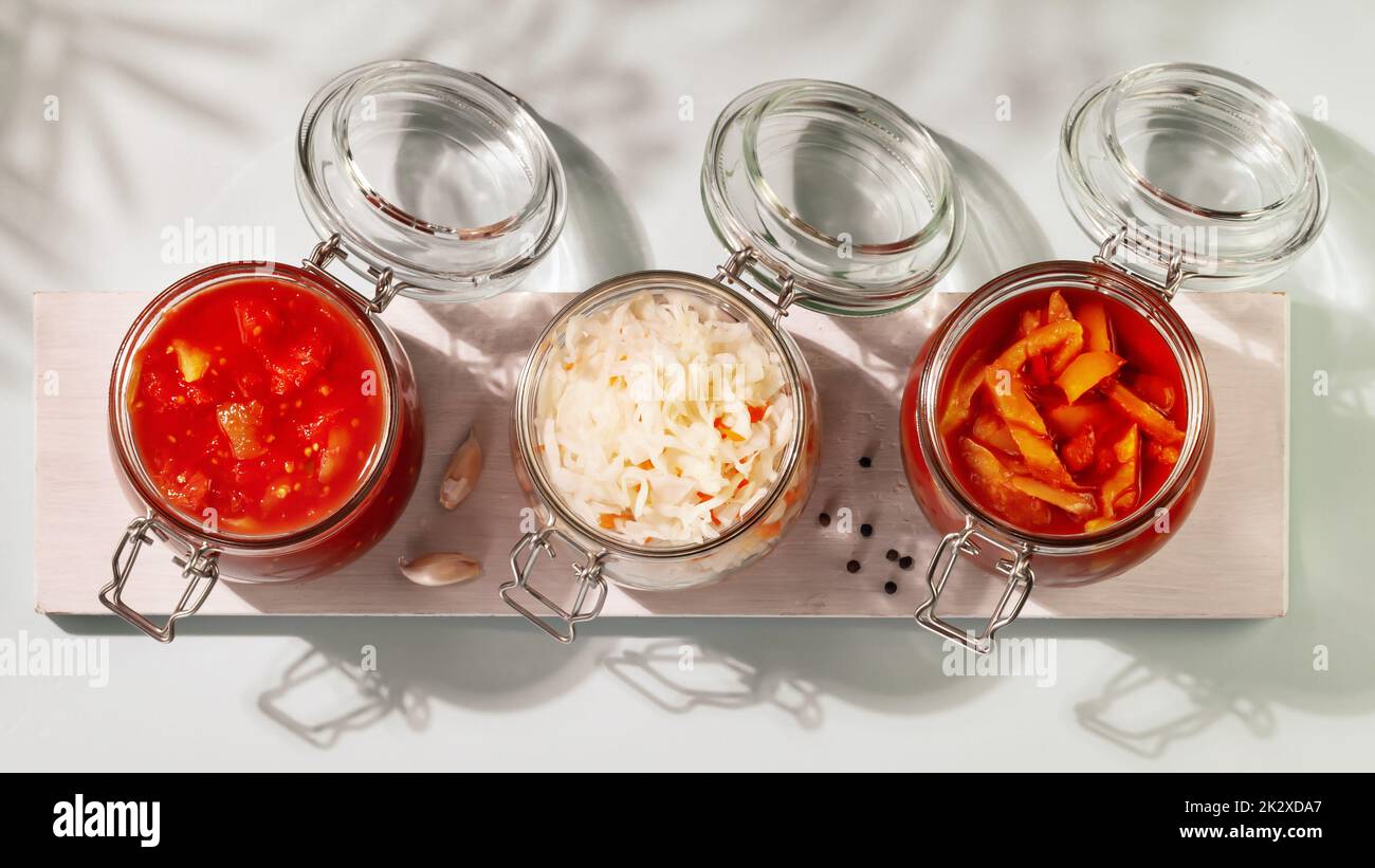 Probiotic food. Pickled or fermented vegetables. Lecho, sauerkraut, ajvar in glass jars on a white board on a blue background with shadows. Home food Stock Photo