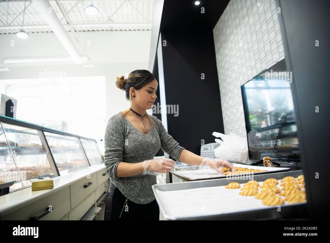 Female pastry shop worker removing pastries from baking sheets Stock