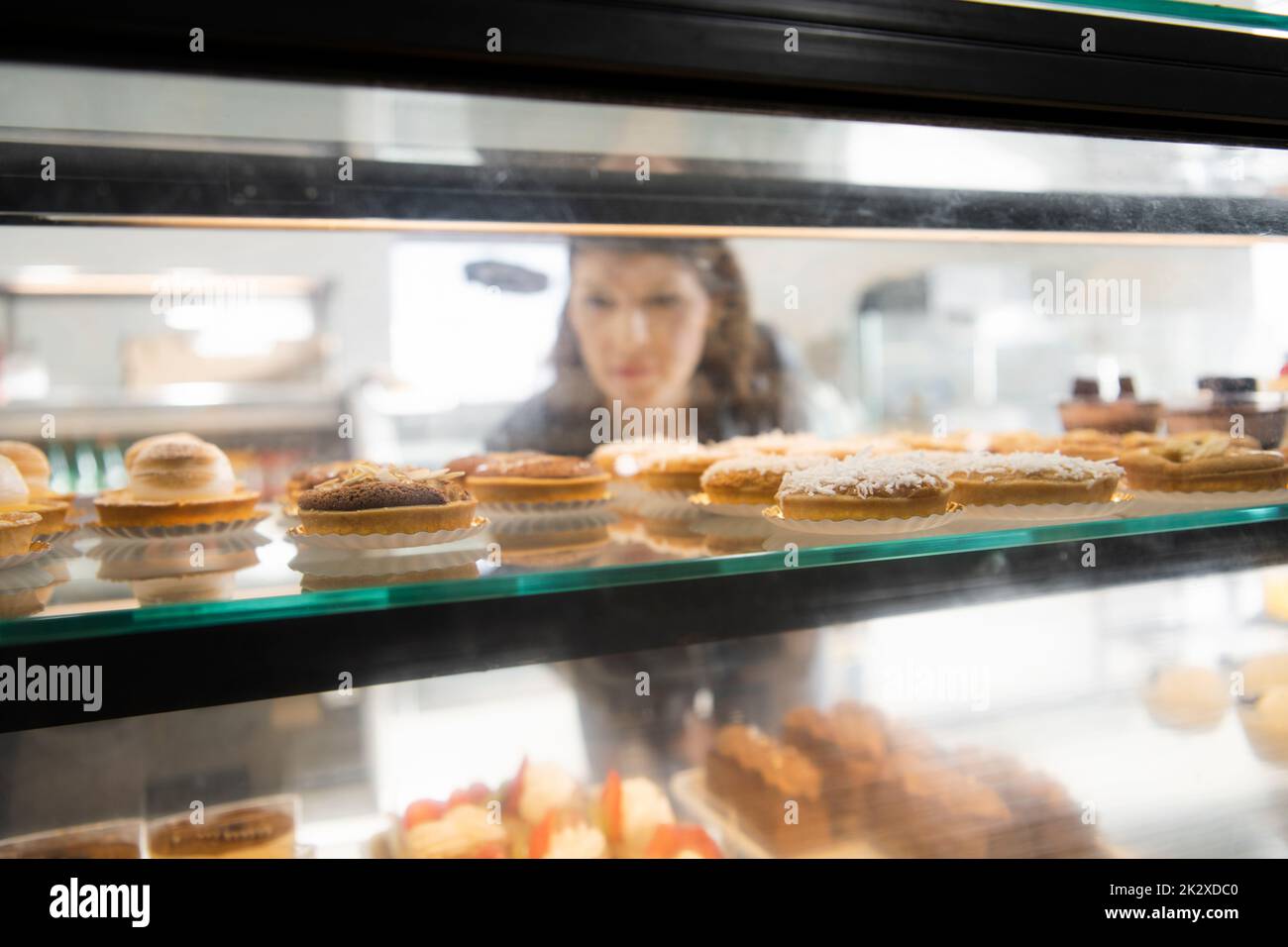 Female customer browsing French pastries in bakery display case Stock