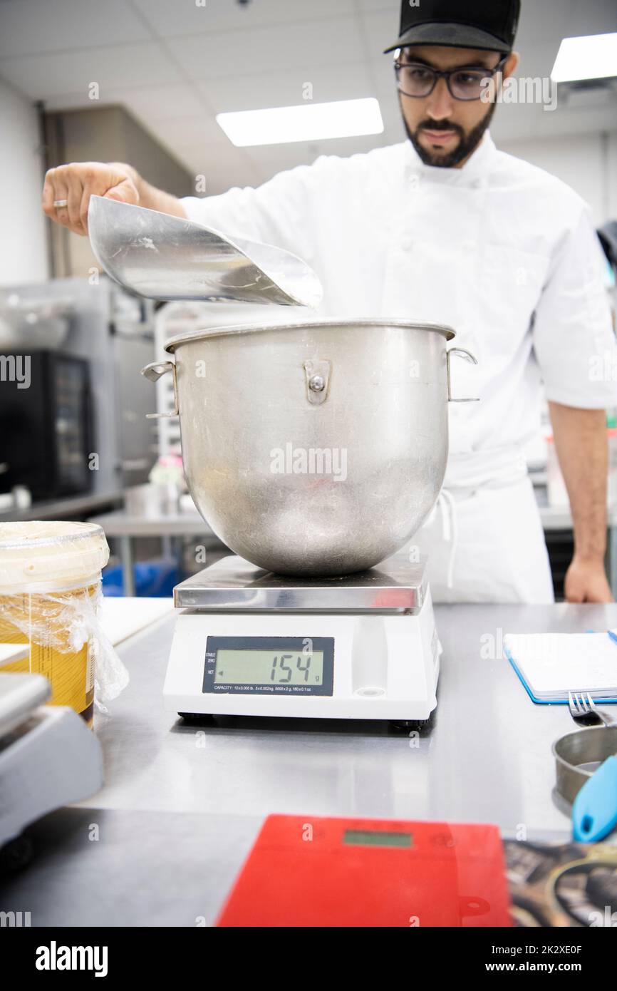 Male baker measuring ingredients at scale in bakery kitchen Stock Photo