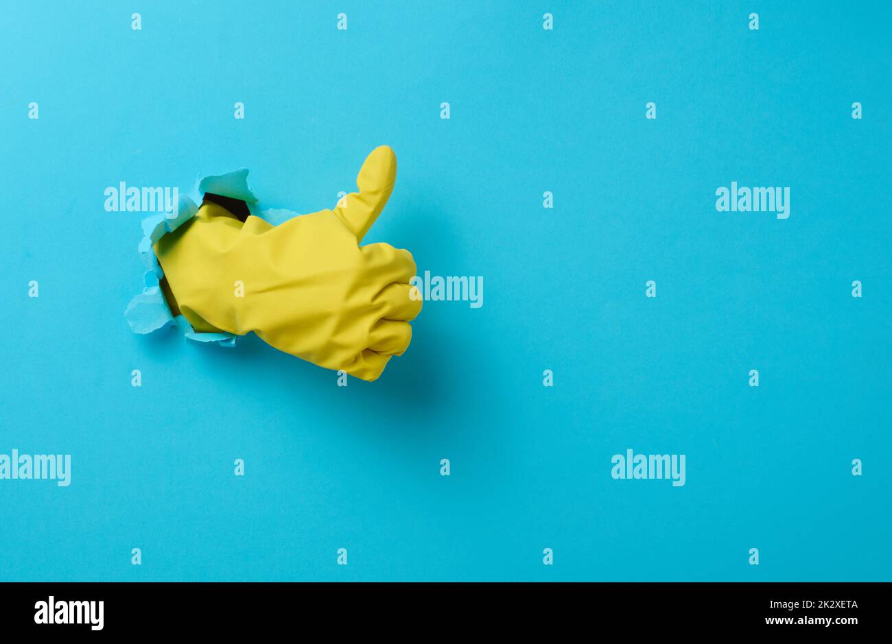 hand in a yellow household rubber glove sticks out of the torn hole and