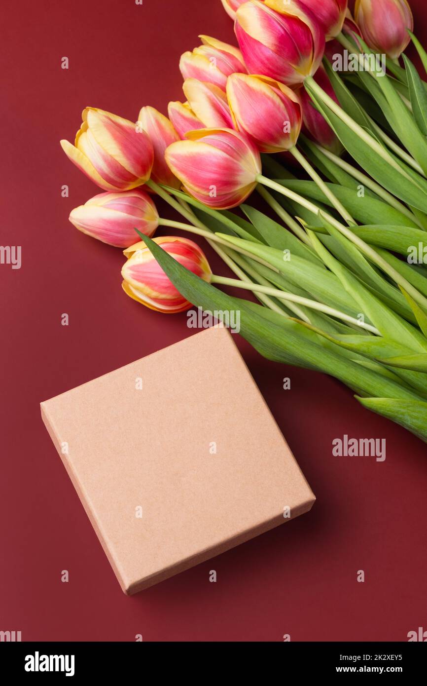 Elegant greeting card with kraft box mockup with tulip bouquet on a burgundy background. Stock Photo
