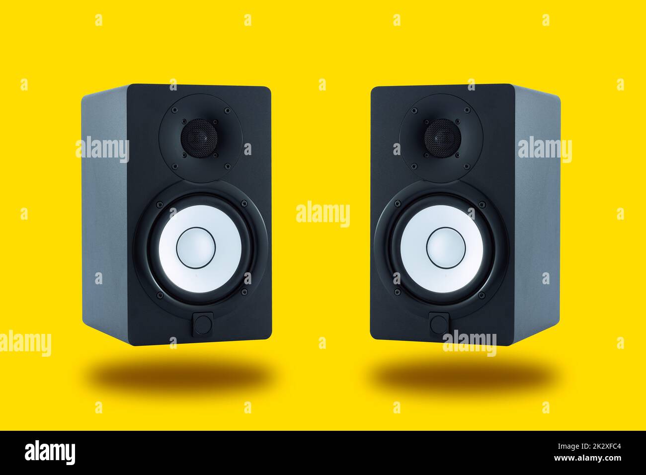 Pair of professional high quality monitor speakers for sound recording, mixing, and mastering in studio in black wooden casing isolated on yellow background. Front or Side view. Stock Photo