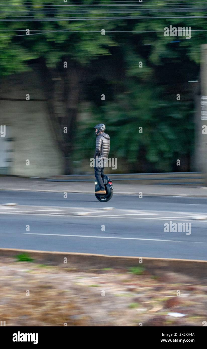 A panning shot of a man driving an electric unicycle on the road wearing a helmet Stock Photo