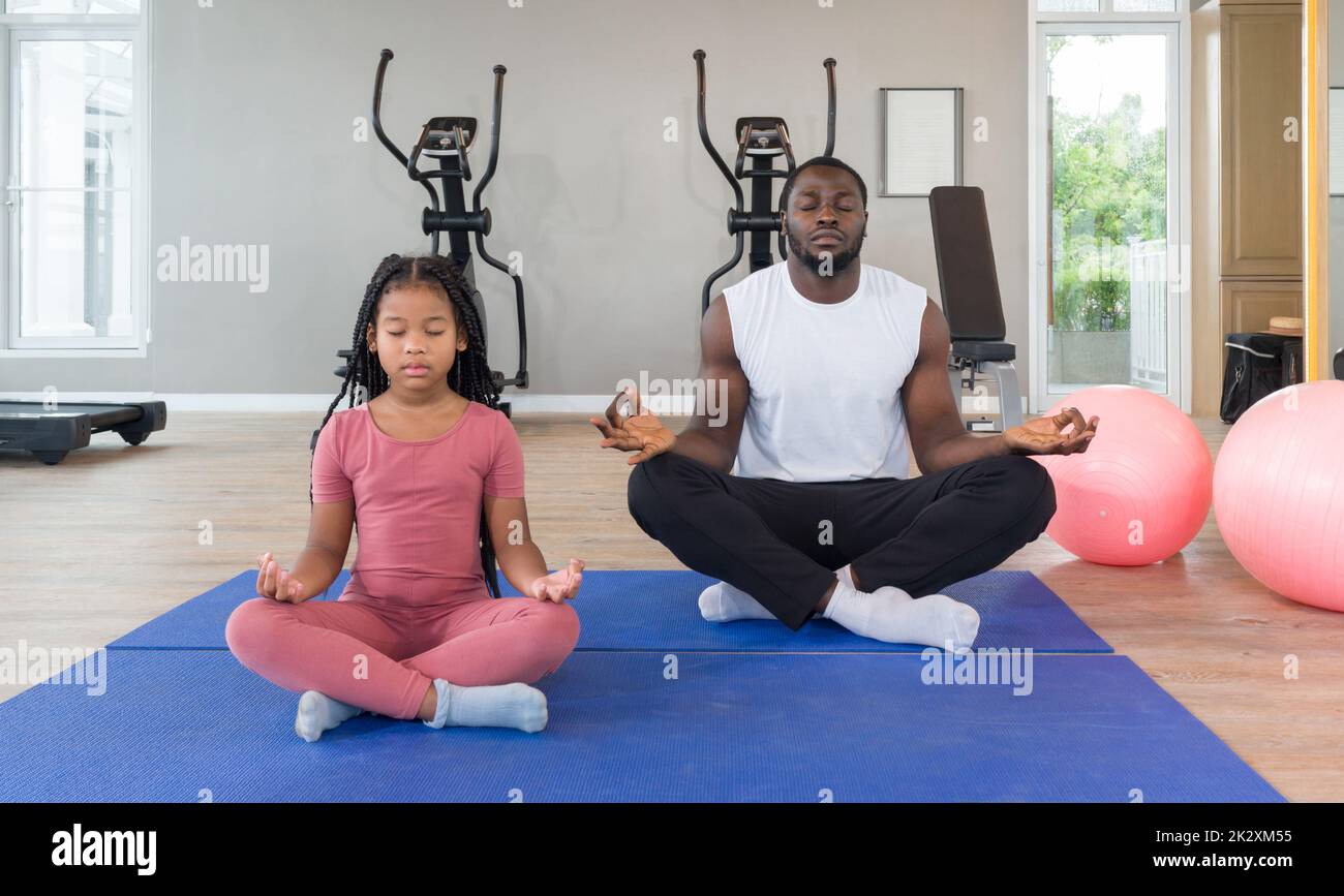 à¸ºBlack Cornrow Braids girl in sportswear meditating with her father on yoga mat before exercise. Two yoga ball are placed next to them. Morning fitness, mindfulness concept. Stock Photo